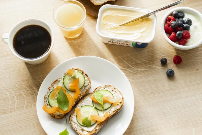 Terveellinen aamupala jossa on kaksi palaa leipää Alentaja levitteellä, marjoja, puuroa, mehua ja kuppi mustaa kahvia