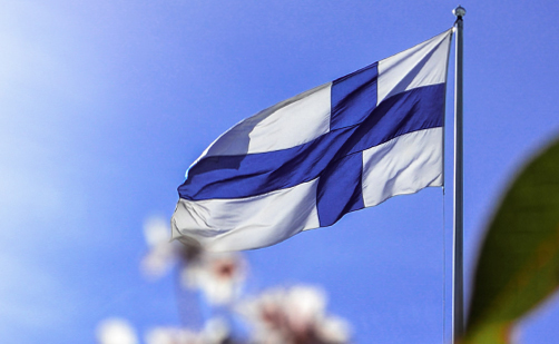 Liehuva suomenlippu pilvetöntä sinistä taivasta vasten etäältä kuvattuna